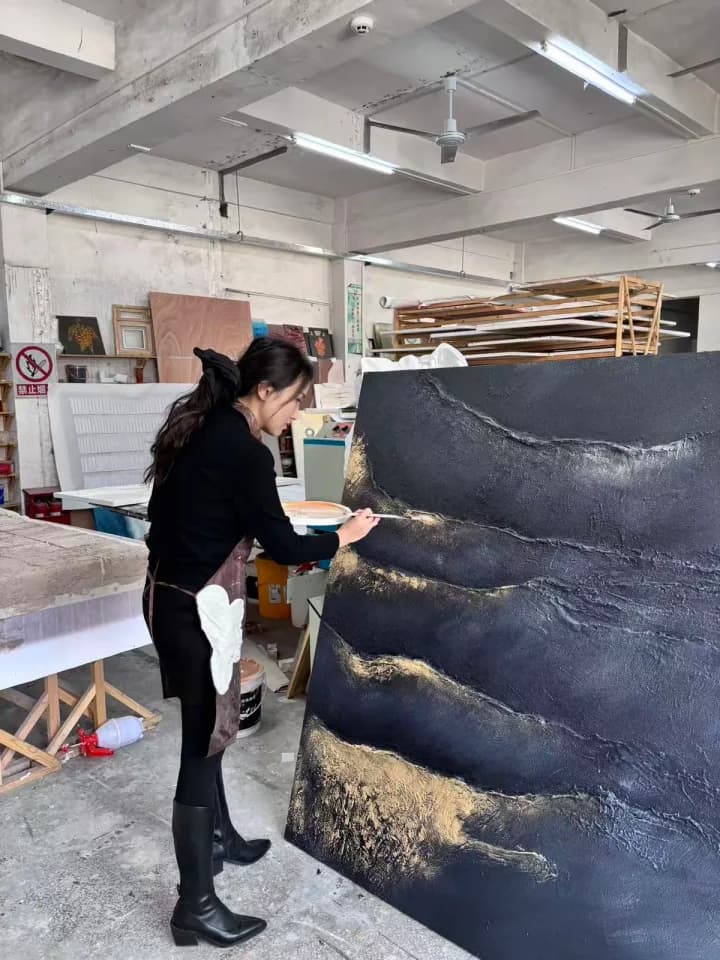 Artist finishing gold details on a large black textured artwork